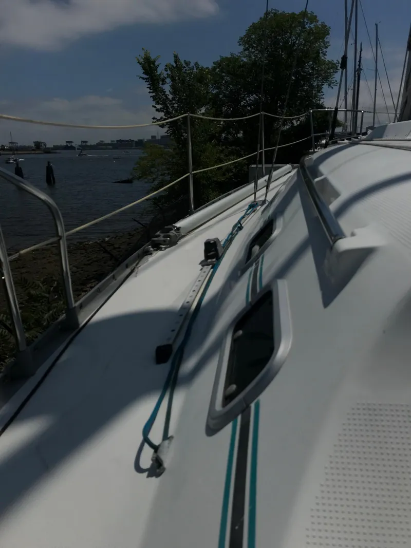 Slide: The Image of 1993 Beneteau First 310 sailboat deck with ropes and railing, near water and trees. - 21