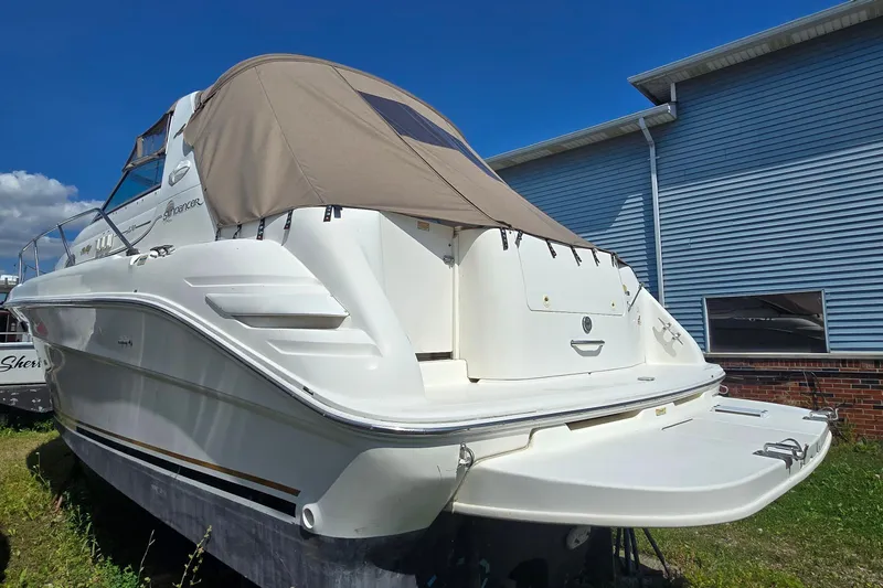 Slide: The Image of 1998 Sea Ray 330 Sundancer boat with beige cover, docked near blue building. - 5