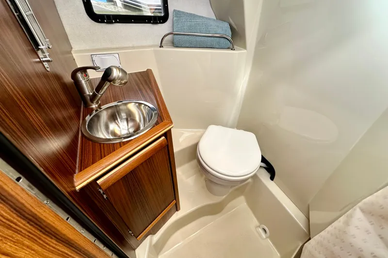 Slide: The Image of 2026 Ranger Tugs R-25 boat bathroom with sink, toilet, and wooden cabinetry. - 32