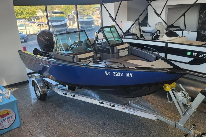 The Image of Blue 2023 Lowe boat on trailer in showroom, surrounded by other boats. - 1