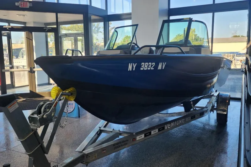 Slide: The Image of Blue Lowe boat on trailer inside showroom, 2023 model, with large windows in background. - 6