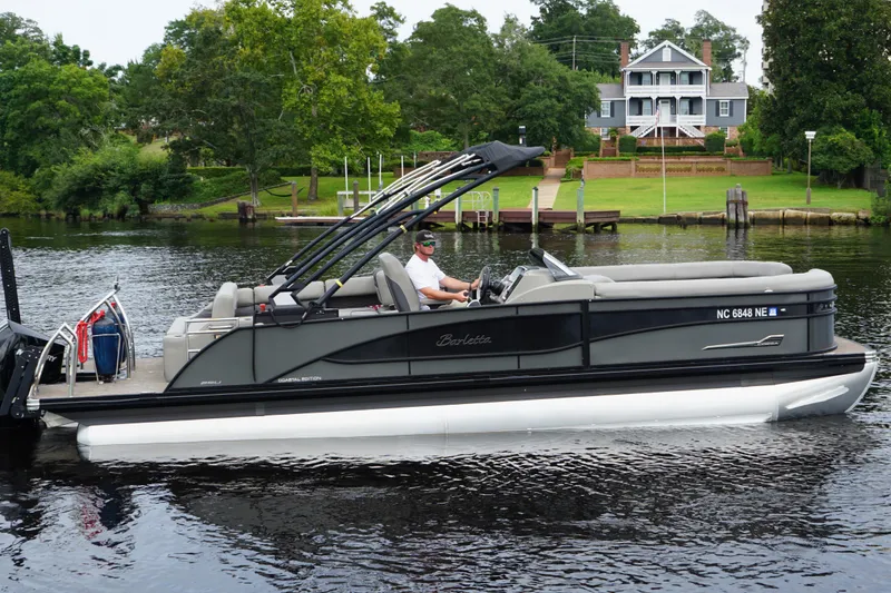 Slide: The Image of 2023 Barletta Corsa 25U pontoon boat cruising on a scenic river near a large house. - 3
