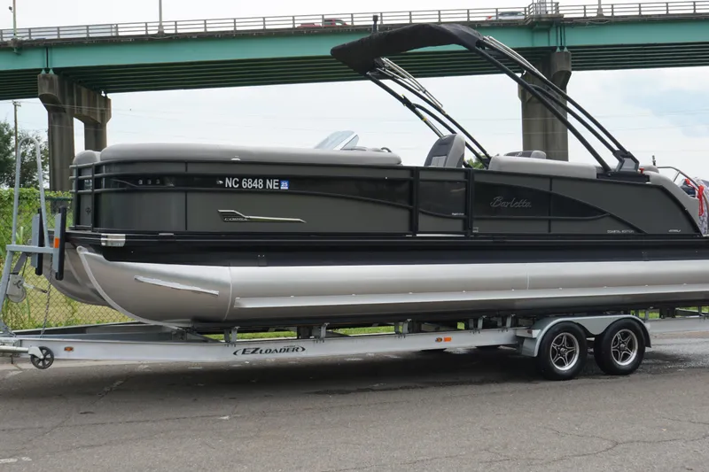 Slide: The Image of 2023 Barletta Corsa 25U pontoon boat on trailer, parked under a bridge. - 6