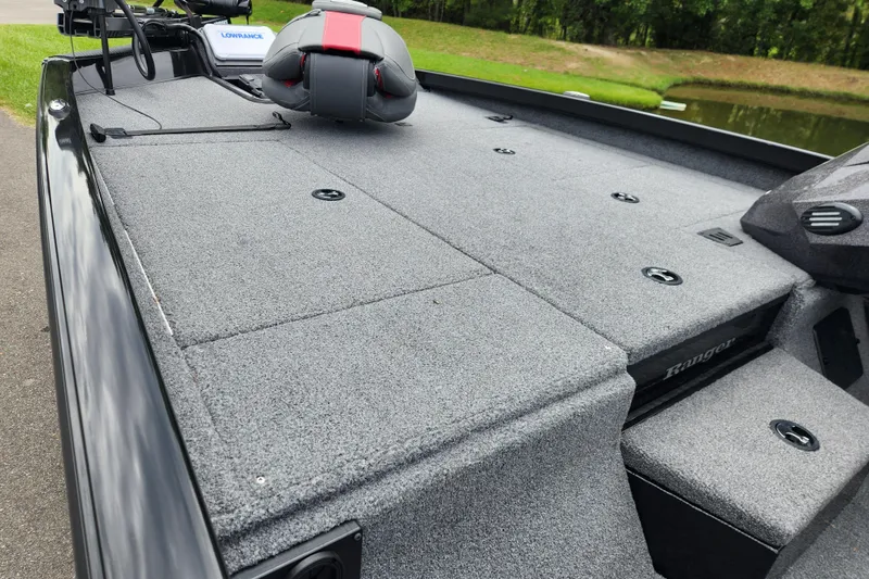 Slide: The Image of 2023 Ranger RT188P boat deck with gray carpet and seating, near a pond. - 7
