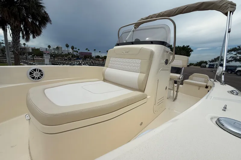 Slide: The Image of 2026 Scout 188 Sportfish boat with beige seating and console, docked under cloudy skies. - 12