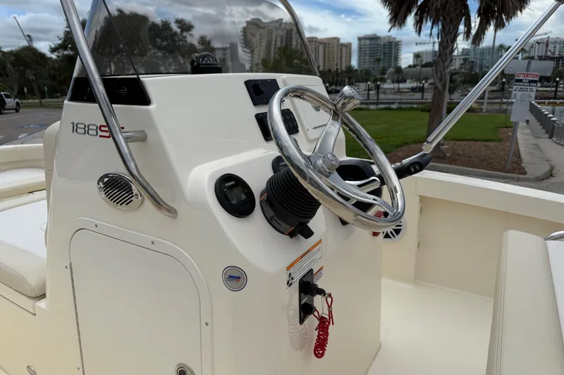 Slide: The Image of 2026 Scout 188 Sportfish boat console with steering wheel and controls, docked near cityscape. - 16