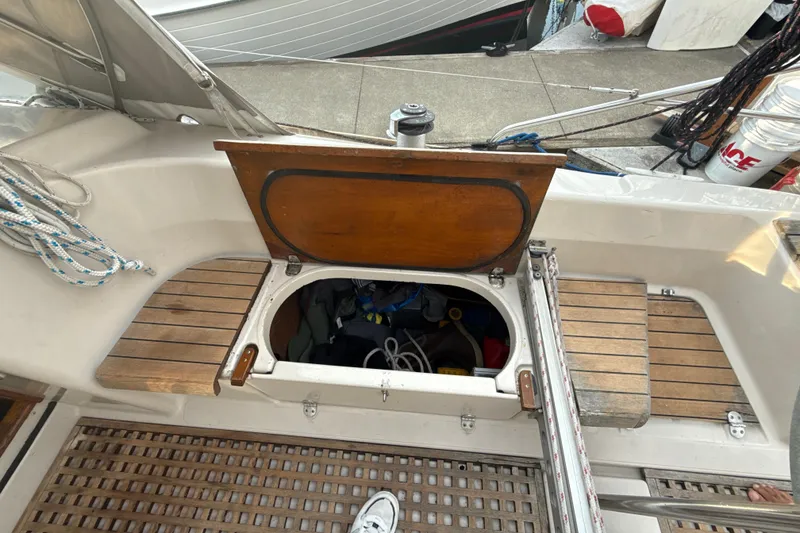 Slide: The Image of 1985 Dehler 372 sailboat cockpit with open storage hatch, wooden seating, and nautical ropes. - 14