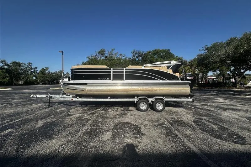 The Image of 2022 Harris Cruiser 230 pontoon boat on a trailer in a parking lot. - 1