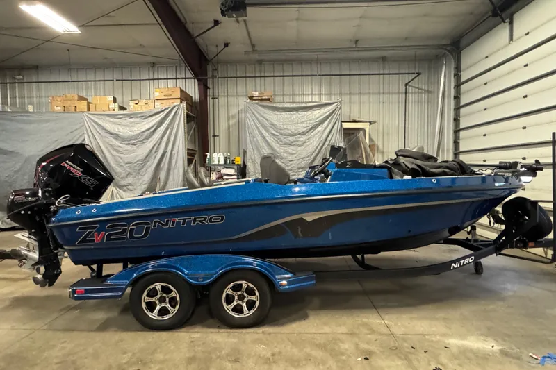Slide: The Image of 2020 Nitro ZV20 Pro fishing boat in a garage, featuring a blue exterior and dual-axle trailer. - 0