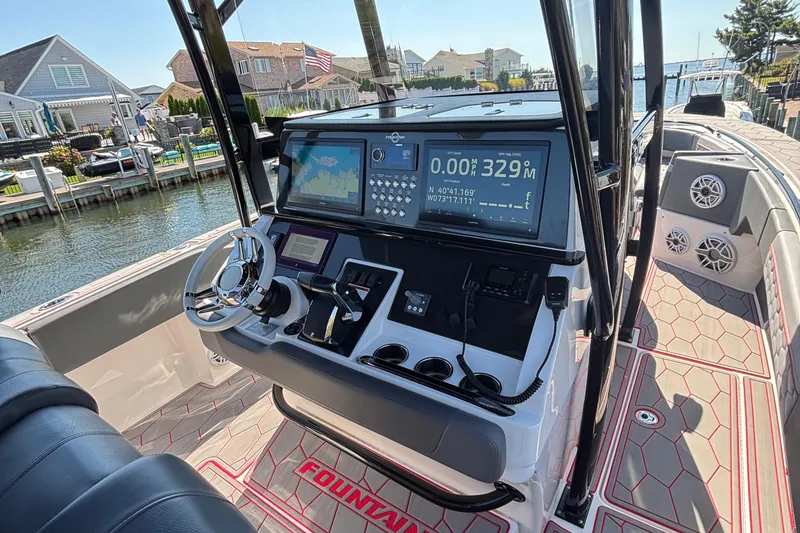 Slide: The Image of 2023 Fountain 34 SC boat dashboard with navigation screens and steering wheel, docked by waterfront homes. - 19