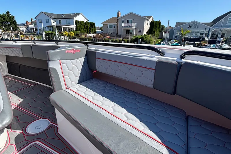 Slide: The Image of 2023 Fountain 34 SC boat interior with stylish gray and red seating, docked near waterfront homes. - 40