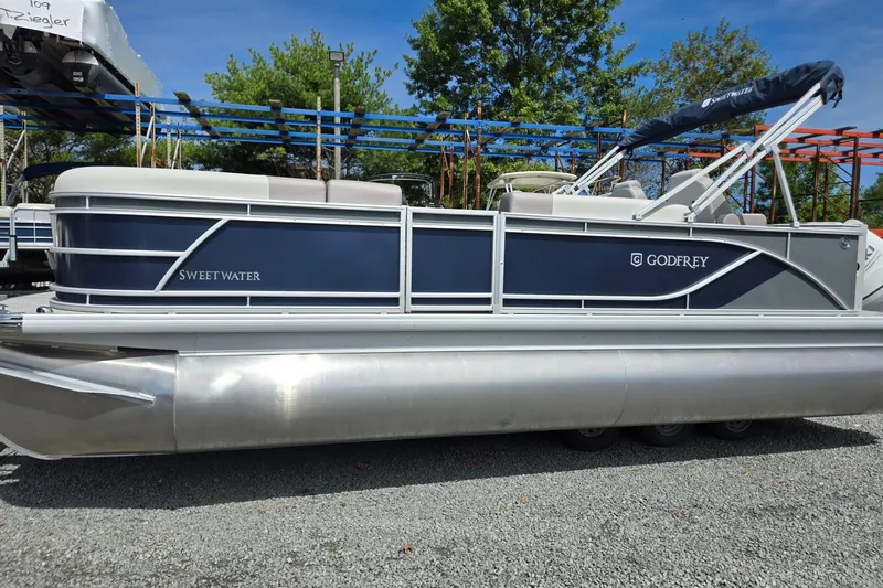 Slide: The Image of 2026 Godfrey Sweetwater 2286 FS pontoon boat, blue and silver, parked on gravel. - 1