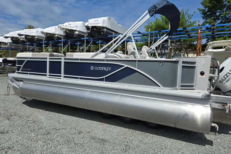Slide: The Image of 2026 Godfrey Sweetwater 2286 FS pontoon boat with Suzuki outboard motor, parked on gravel. - 2