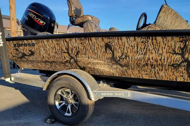 The Image of 2026 Xpress XP180 boat with camouflage design on a trailer, featuring a powerful outboard motor. - 1