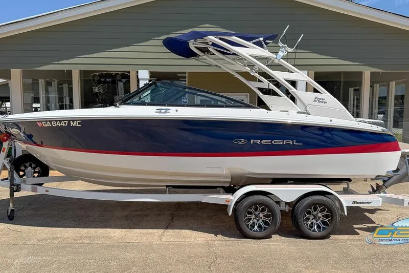 Slide: The Image of 2022 Regal LS2 Surf boat on trailer, blue and white design, parked outdoors. - 1