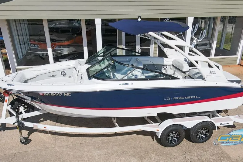 Slide: The Image of 2022 Regal LS2 Surf boat on trailer, blue and white design, parked outside. - 11