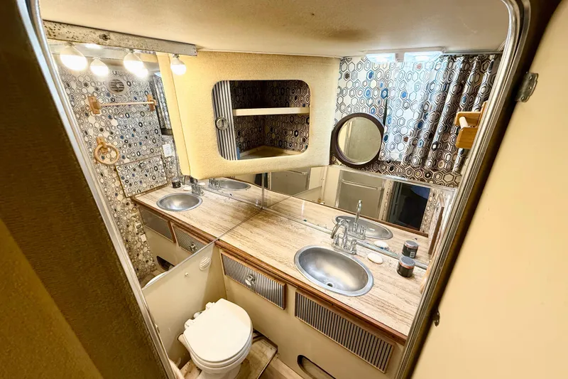 Slide: The Image of 1982 Chris-Craft 410 Motor Yacht bathroom with dual sinks, patterned wallpaper, and round mirror. - 13