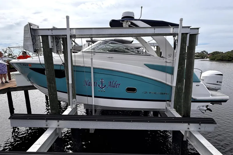 Slide: The Image of 2021 Regal 26 XO boat on lift, turquoise and white design, docked by water. - 2