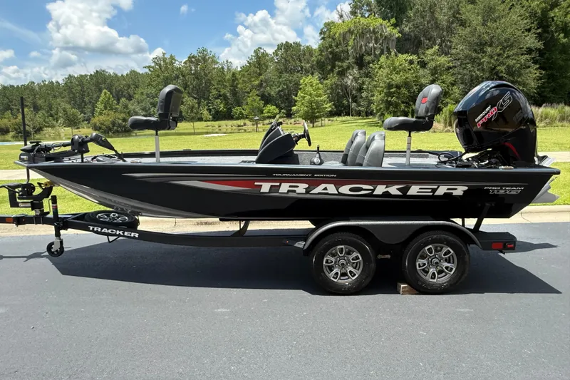 The Image of 2026 Tracker Pro Team 195 boat on trailer, parked outdoors, with lush greenery in the background. - 0