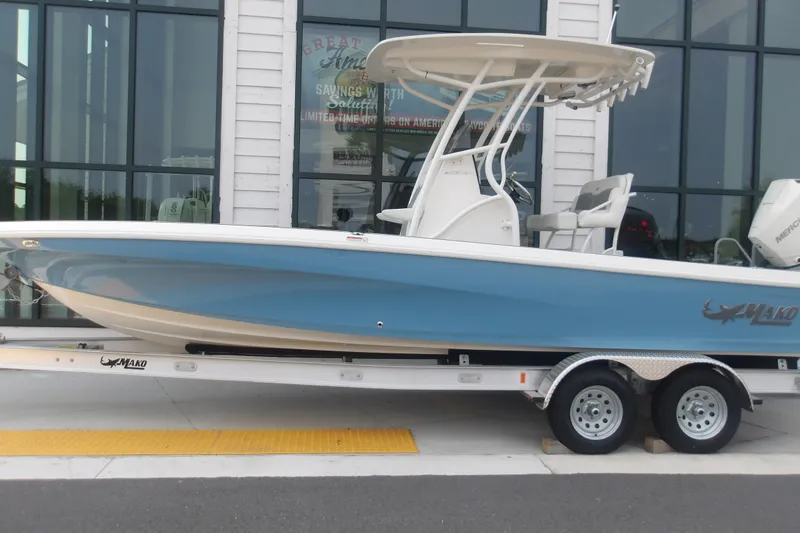 Slide: The Image of 2026 Mako 24 APEX boat on trailer, blue hull, parked outside showroom. - 1