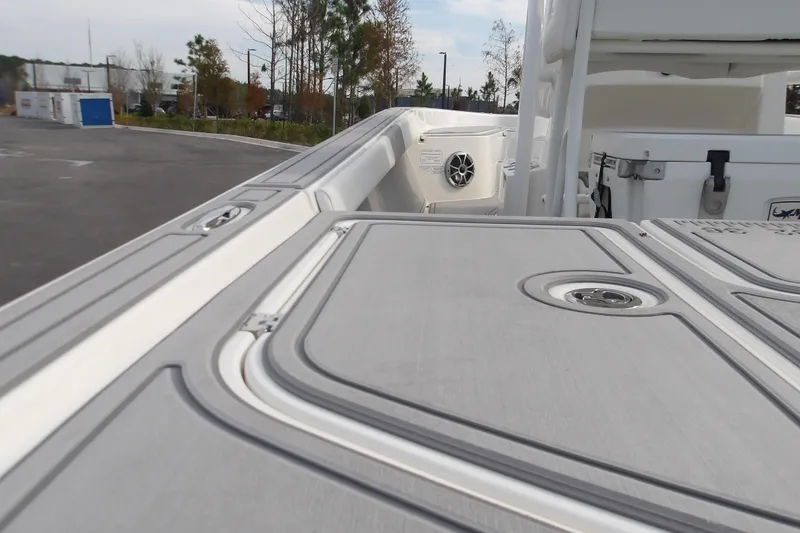 Slide: The Image of 2026 Mako 24 APEX boat deck with storage compartments and speaker, parked outdoors. - 19