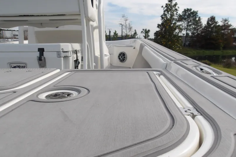 Slide: The Image of 2026 Mako 24 APEX boat deck with storage compartments and cooler, surrounded by greenery. - 20