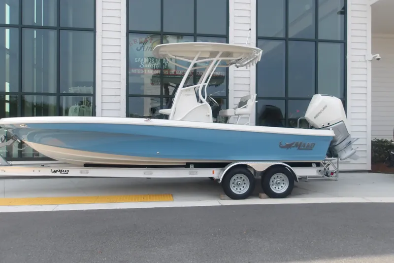 The Image of 2026 Mako 24 APEX boat on trailer, blue hull, parked outside a building. - 0