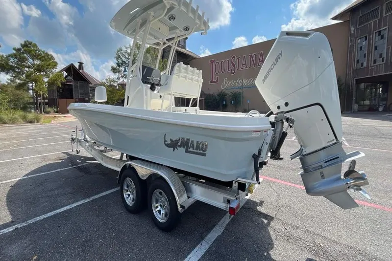 Slide: The Image of 2026 Mako 24 APEX boat on trailer, parked in a lot with trees and building nearby. - 2
