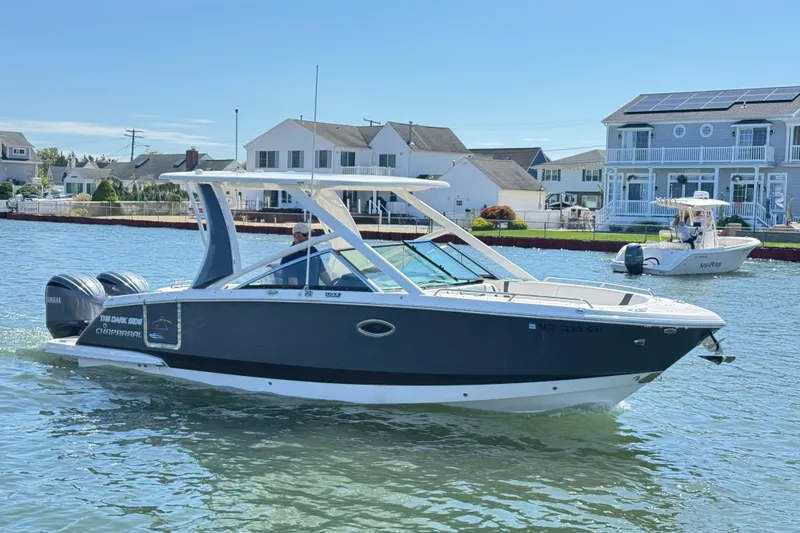 Slide: The Image of 2022 Chaparral 280 OSX boat cruising on a sunny waterfront near houses. - 2