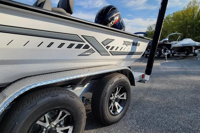 The Image of 2026 Xpress H18 Bass boat on trailer, showcasing sleek design and dual wheels. - 1