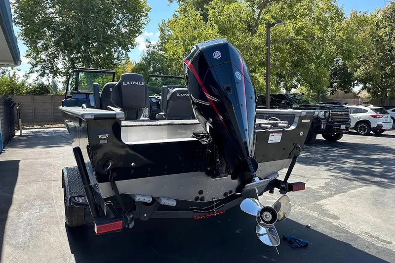 Slide: The Image of 2025 Lund 1875 Pro-V boat with outboard motor, parked outdoors on a sunny day. - 10