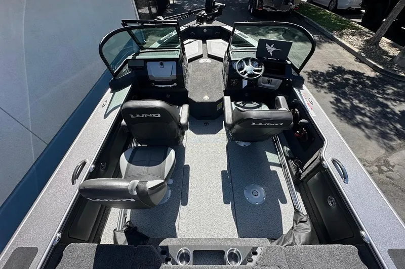 Slide: The Image of 2025 Lund 1875 Pro-V boat interior with seating and steering console, parked outdoors. - 11