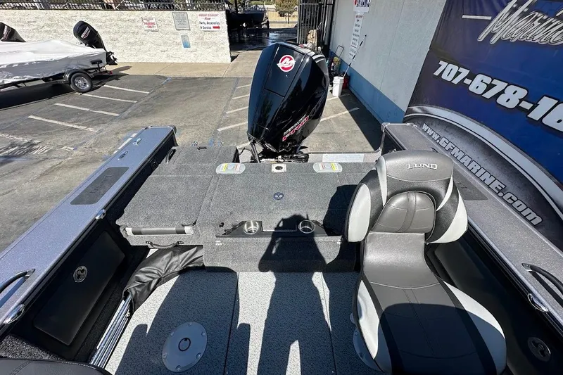 Slide: The Image of 2025 Lund 1875 Pro-V boat interior with seating and motor, parked at a dealership. - 12