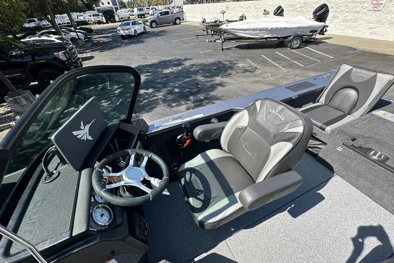 Slide: The Image of 2025 Lund 1875 Pro-V boat interior with steering wheel and seating in a parking lot. - 21