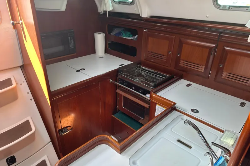 Slide: The Image of 2004 Beneteau 361 yacht kitchen with stove, microwave, and wooden cabinetry. - 27