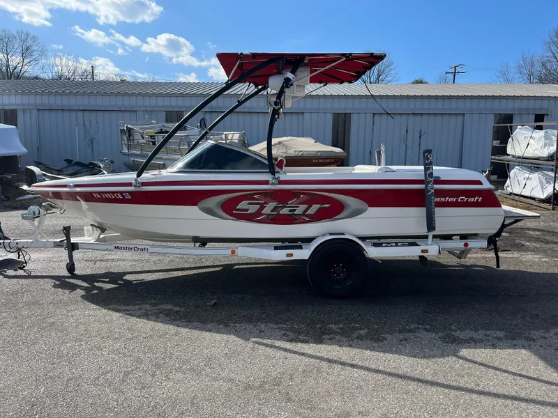 Slide: The Image of 1999 MasterCraft XStar boat with red and white design on a trailer, parked outdoors. - 11