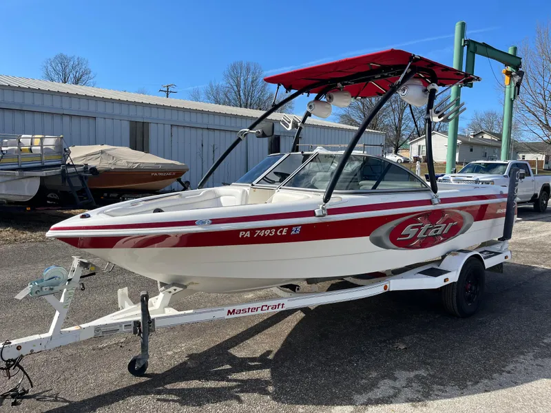 Slide: The Image of 1999 MasterCraft XStar boat with red accents on a trailer, parked outdoors. - 12