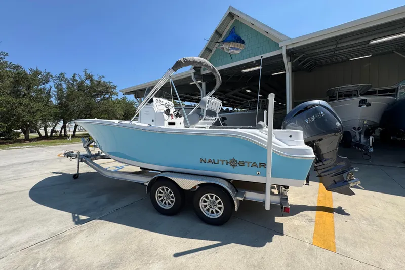 Slide: The Image of 2026 NauticStar 212 Legacy boat on trailer, parked outdoors near a boat shed. - 15