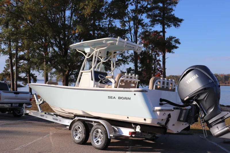Slide: The Image of 2024 Sea Born LX24 Center Console boat on trailer by lake, featuring Yamaha engine. - 10