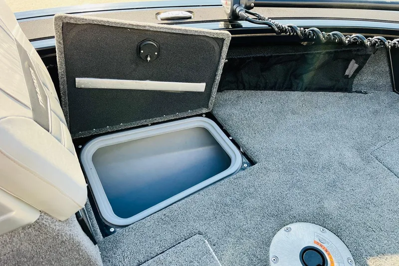 Slide: The Image of 2018 Tracker Targa V-19 Combo boat storage compartment, open lid, gray interior. - 18
