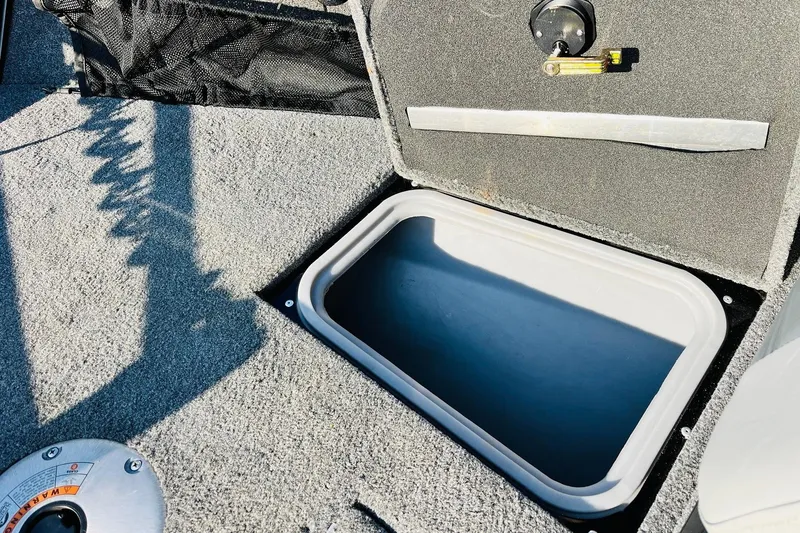 Slide: The Image of 2018 Tracker Targa V-19 Combo storage compartment, open lid, gray carpeted interior. - 22