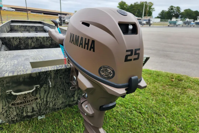 Slide: The Image of 2026 Tracker Grizzly 15 Jon boat with Yamaha 25 outboard motor, parked on grass. - 3