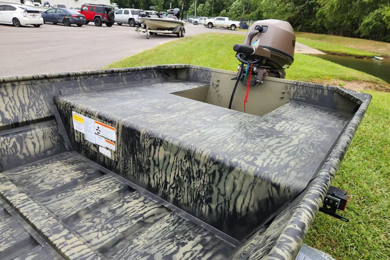 Slide: The Image of 2026 Tracker Grizzly 15 Jon boat with camouflage design and outboard motor in parking area. - 5