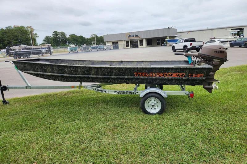Slide: The Image of 2026 Tracker Grizzly 15 Jon boat on trailer, parked on grass near dealership. - 7