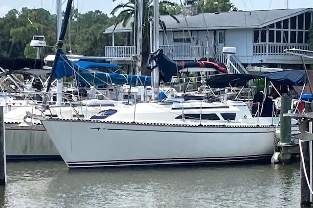 The Image of 1990 C&C 30-2 sailboat docked at a marina with surrounding boats and waterfront house. - 0