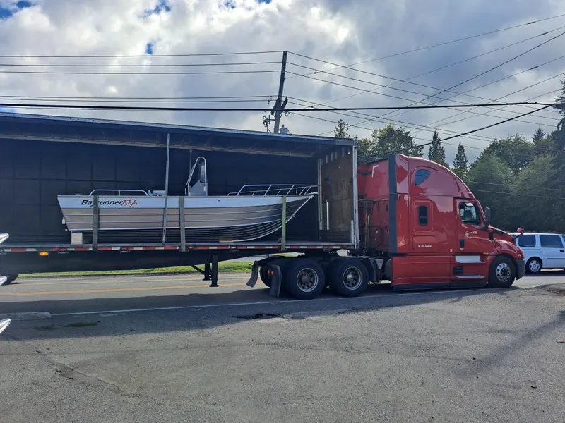 The Image of Red truck transporting 2025 Klamath Baja Bayrunner boat on a flatbed trailer. - 0