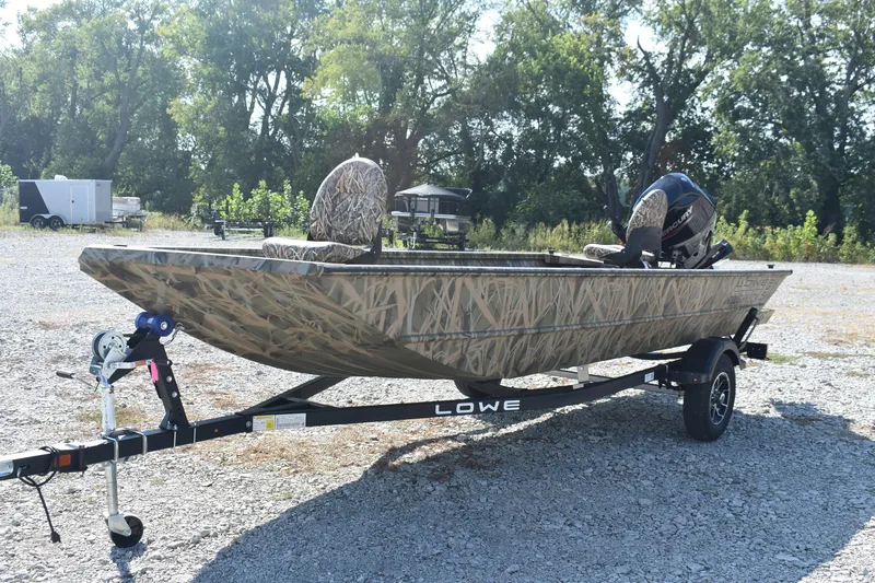 Slide: The Image of 2026 Lowe Roughneck 1860 boat with camouflage design on a trailer in a gravel lot. - 3