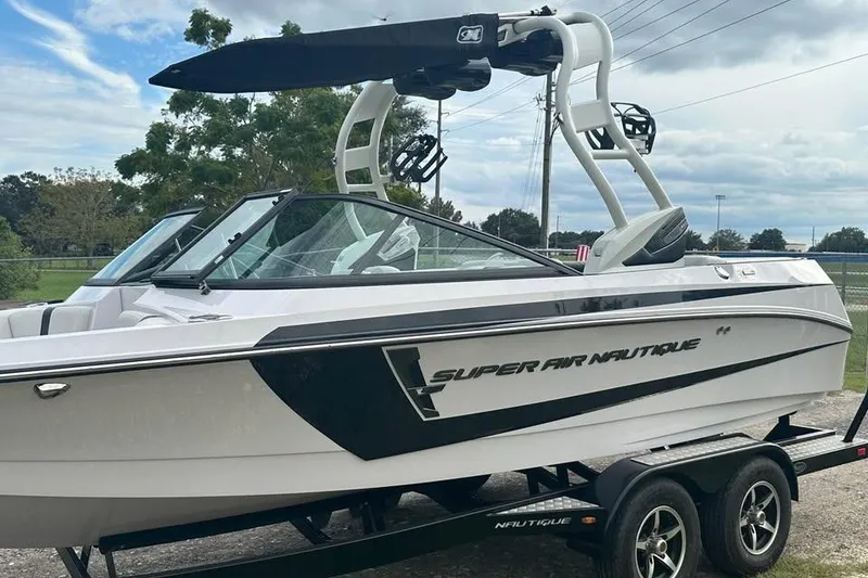 Slide: The Image of 2015 Nautique Super Air Nautique 210 boat on trailer, sleek design, white and black exterior. - 14