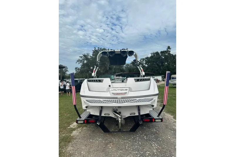 Slide: The Image of 2015 Nautique Super Air Nautique 210 boat, rear view, parked on grass under cloudy sky. - 15