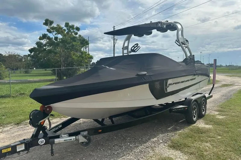 Slide: The Image of 2015 Nautique Super Air Nautique 210 boat on trailer, covered, parked outdoors. - 2